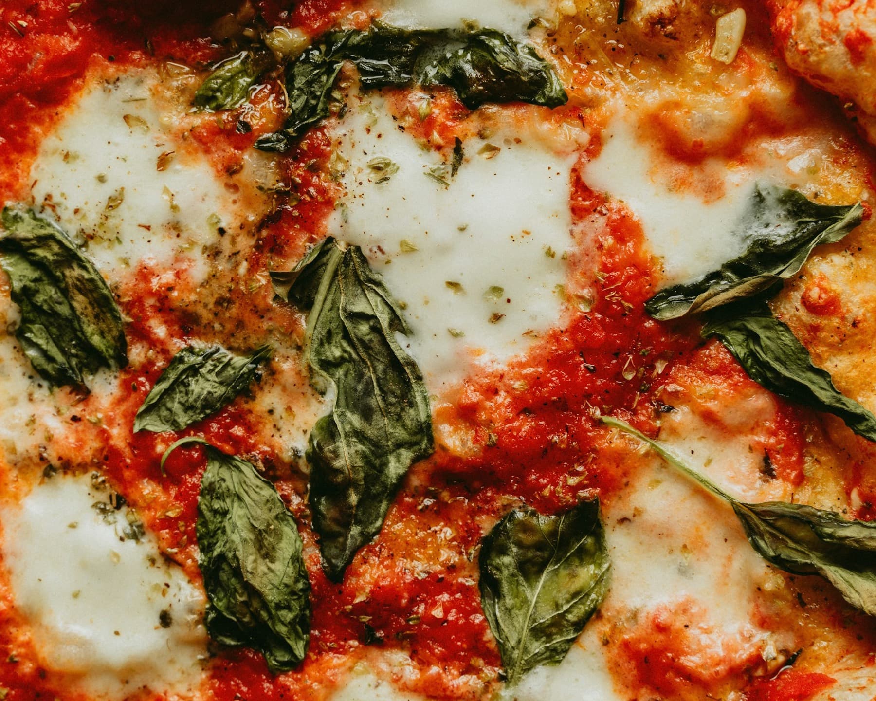 Pizza Margherita vue de près : sauce tomate, mozzarella fondue, feuilles de basilic.