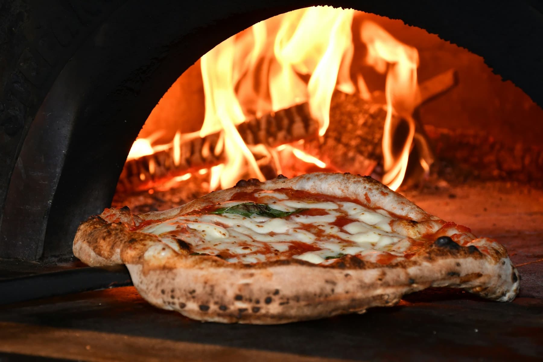 Margherita qui cuit dans le four à bois, les flammes juste derrière la croûte.